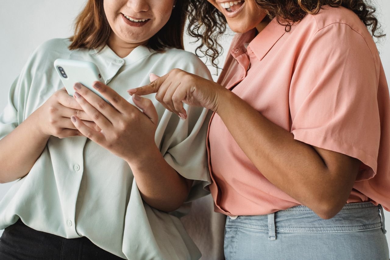 Nosotros Close-up of two women interacting with a smartphone, smiling and engaging with technology.